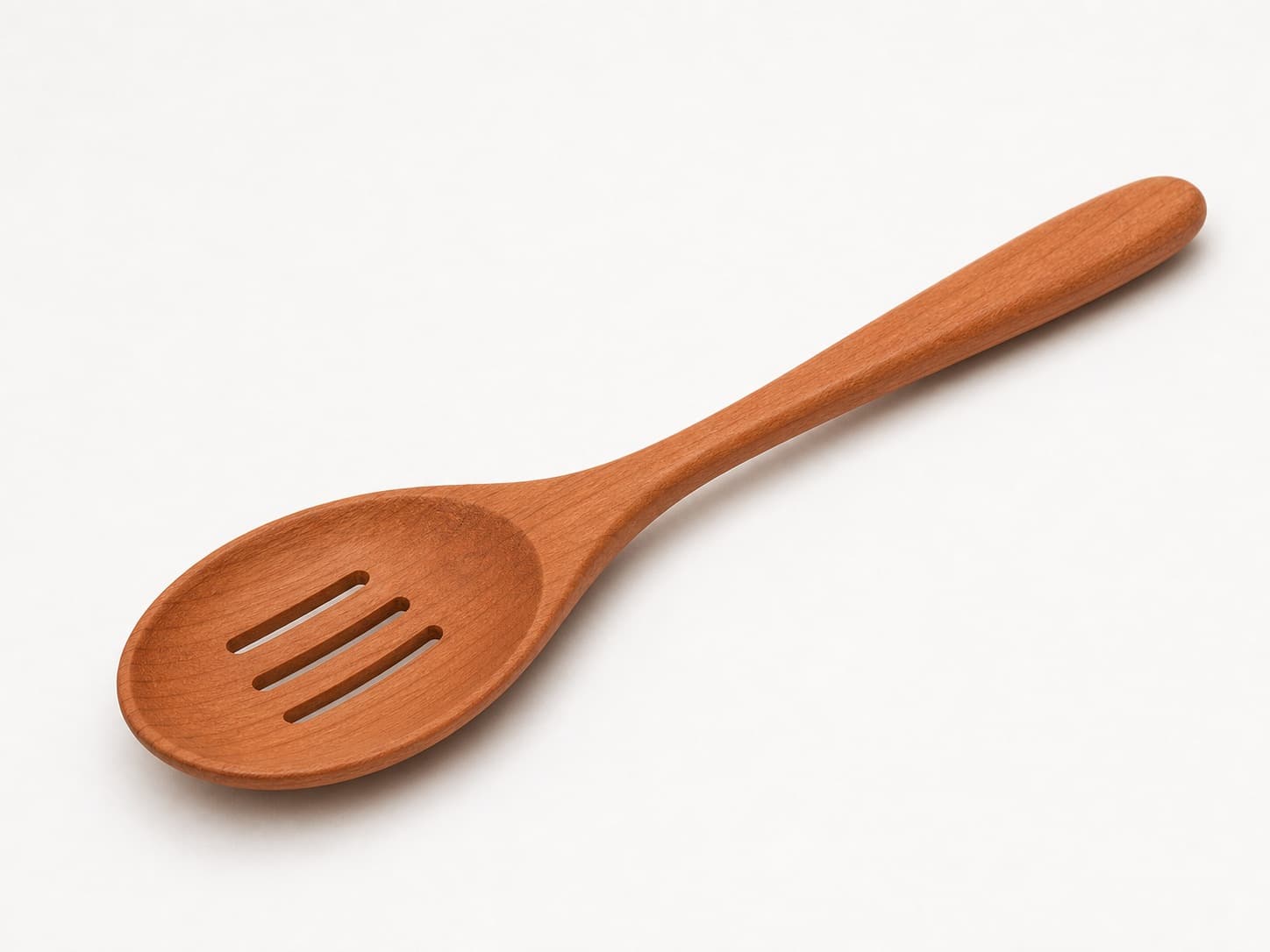 Slotted cooking spoon with warm red-brown grain shown in cherry