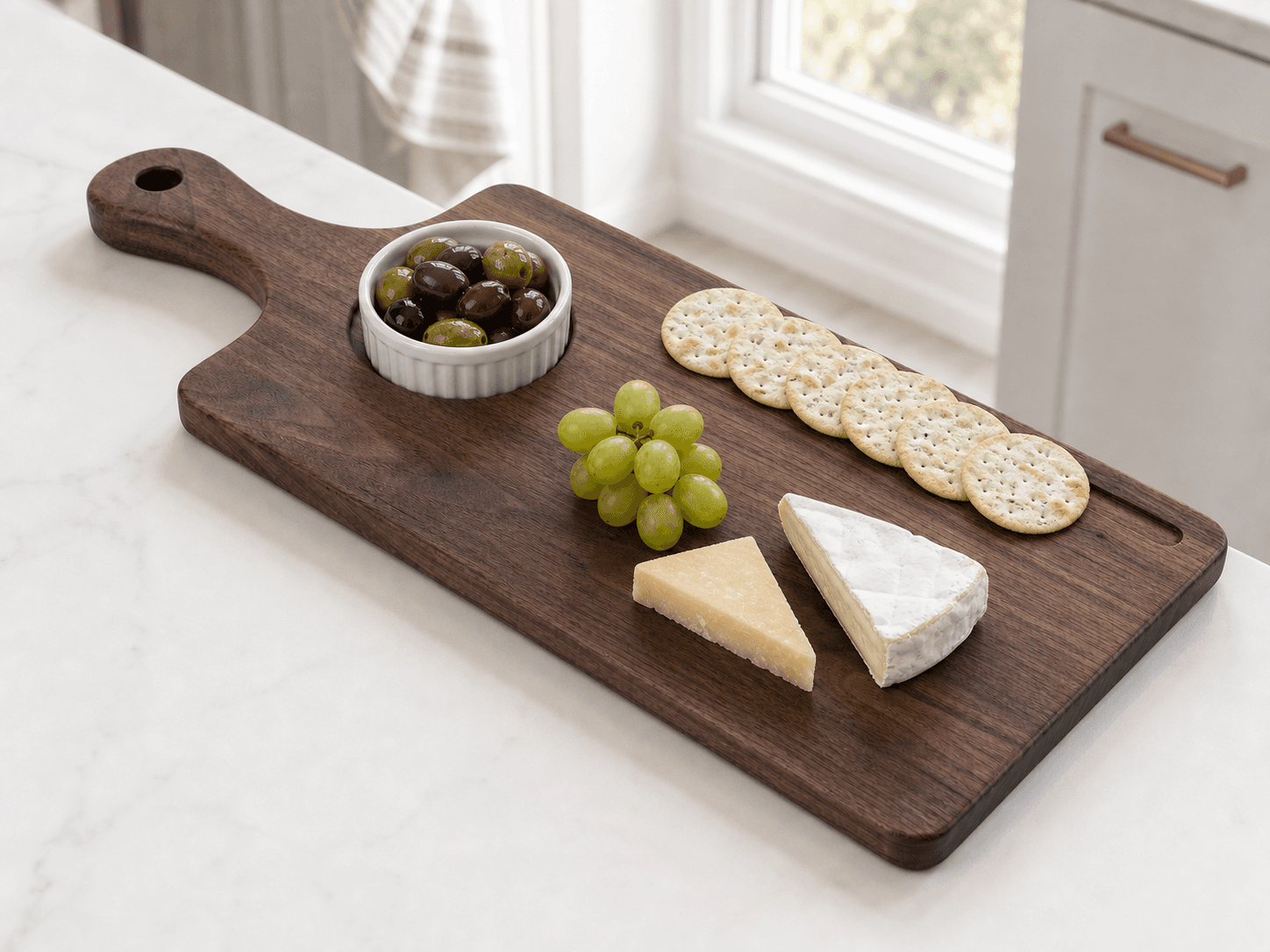 Walnut paddle serving crackers, cheese, grapes, and olives